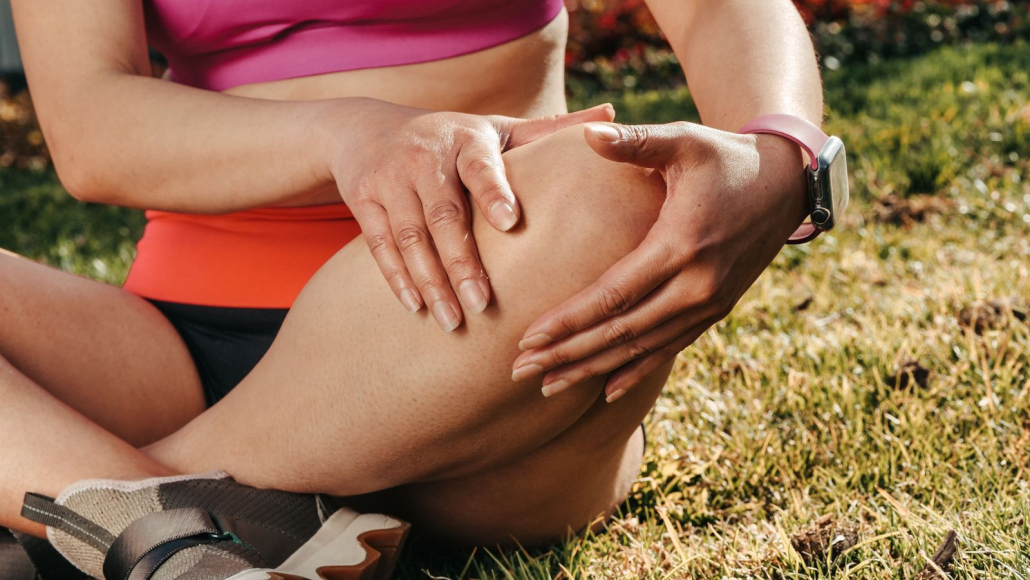 Deportista sentada en el césped sujetándose la rodilla con las dos manos
