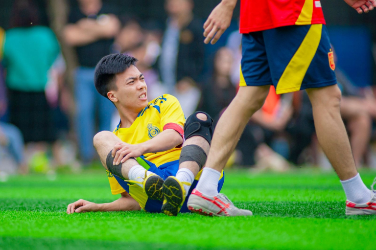 Futbolista amateur sentado en el césped sujetándose la rodilla tras una lesión durante el partido